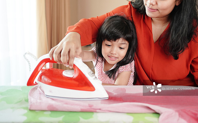 幸福亚细亚家庭的妈妈和小女儿一起在家里从事家务熨烫衣服熨烫。衣服的概念图片素材