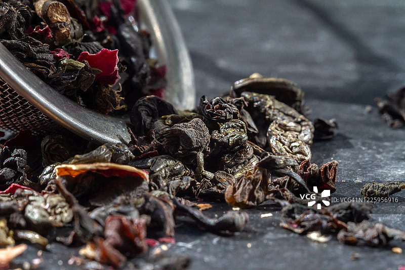 绿茶和红茶的茶叶躺在一个铁筛茶壶中，映衬着黑色的背景图片素材