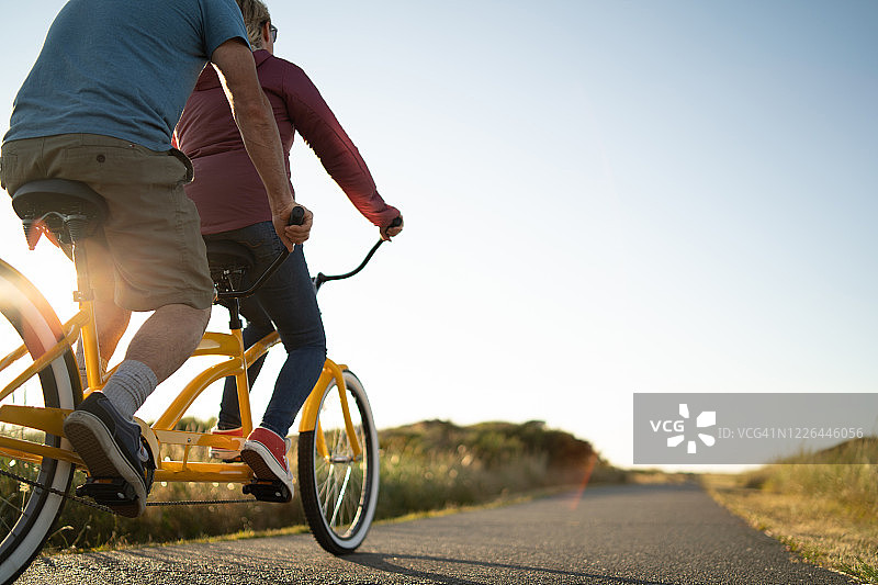 一对夫妇在日出时沿着小路骑双人自行车图片素材