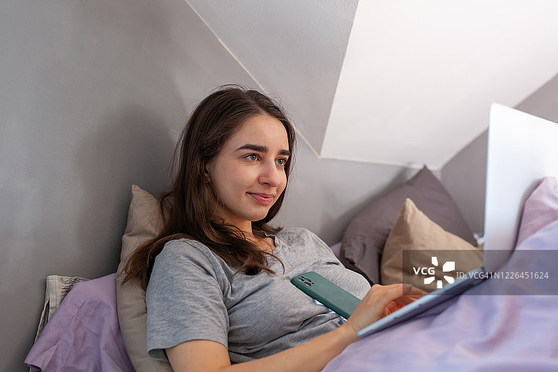 微笑的女人正在床上用笔记本电脑工作图片素材