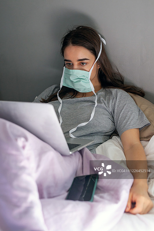 戴着口罩在床上用笔记本电脑工作的女人图片素材