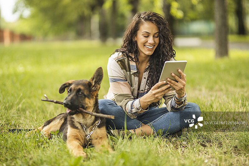 一个女人在公园里用着平板电脑，坐在狗旁边图片素材