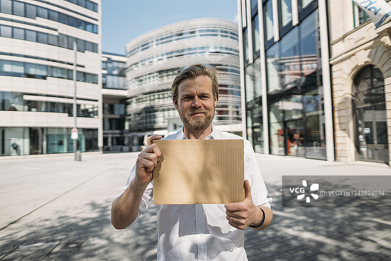 一个微笑的男人在城市里拿着空白纸板的肖像图片素材