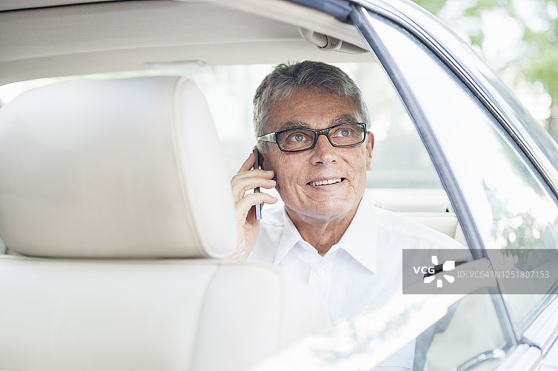 肖像微笑的资深商人在电话看汽车窗外的车图片素材