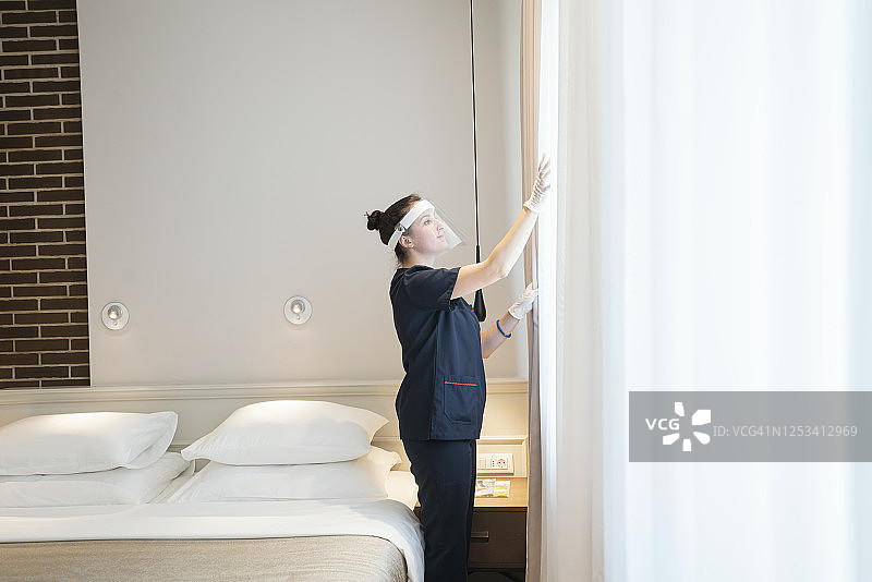 在酒店工作的女服务员戴着面具在拉窗帘图片素材