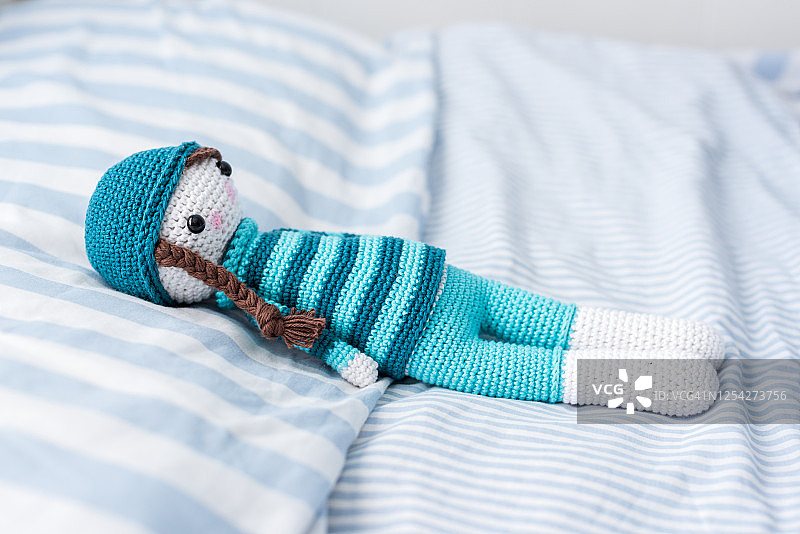 手工钩针娃娃在蓝色与帽子在床上图片素材