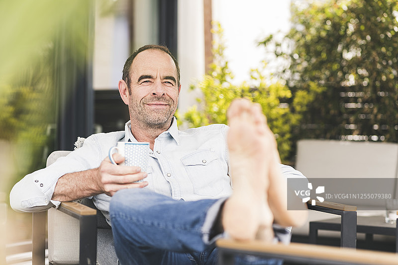 微笑的男人坐在后院，拿着咖啡杯图片素材