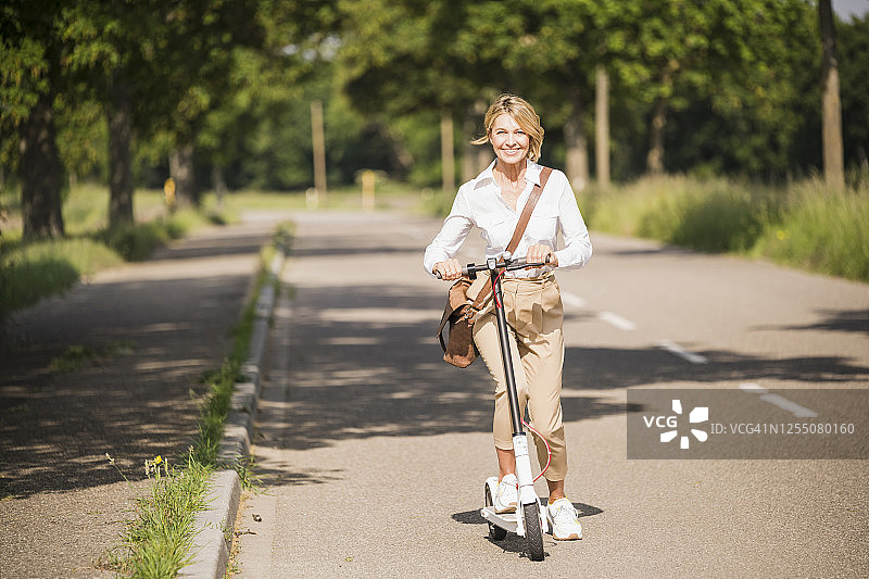 快乐的女商人在阳光明媚的日子里骑着电动踏板车上下班图片素材