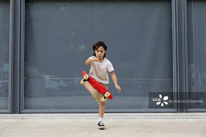 靠墙站在人行道上练习滑板特技的男孩图片素材