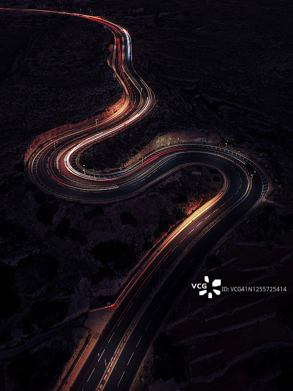 鸟瞰图蜿蜒的道路在夜间时间。在一条s形的乡村公路上，车灯闪烁着。图片素材