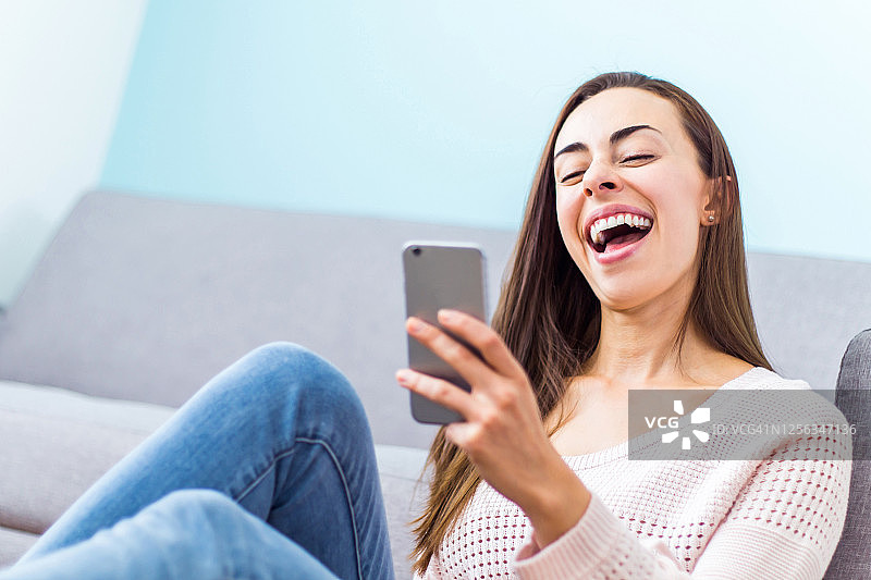 快乐的女人在家里一边拿着手机一边在视频通话中笑图片素材