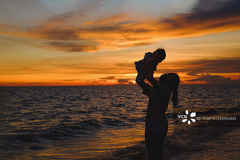 在日落时，母亲在沙滩上的天空中养育婴儿的剪影图片素材