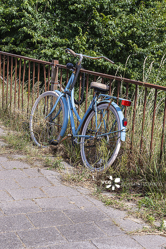 浅蓝色的荷兰老妇人的自行车停在生锈的钢篱笆旁图片素材