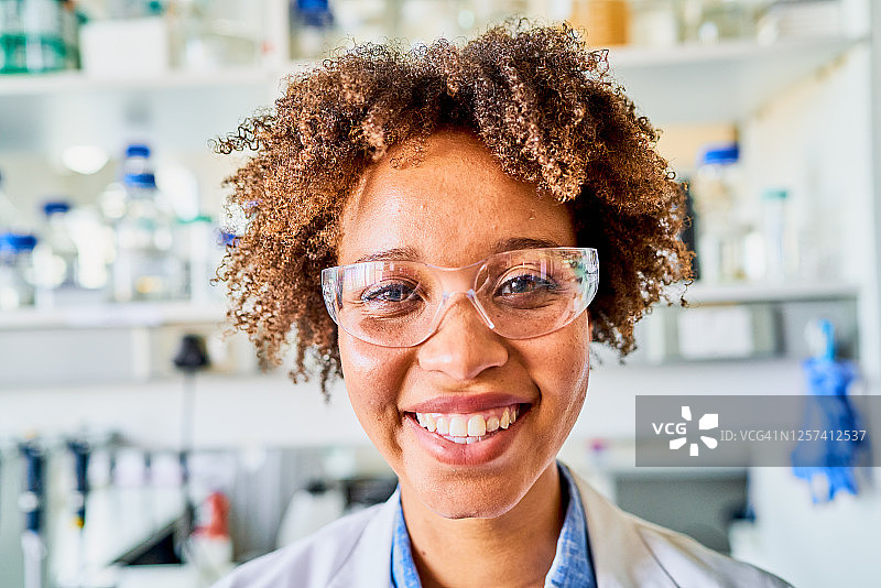 带着保护眼镜微笑的年轻科学家站在实验室里图片素材