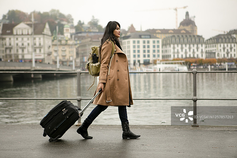 年轻的亚洲女子提着行李箱走在卢塞恩的人行道上图片素材