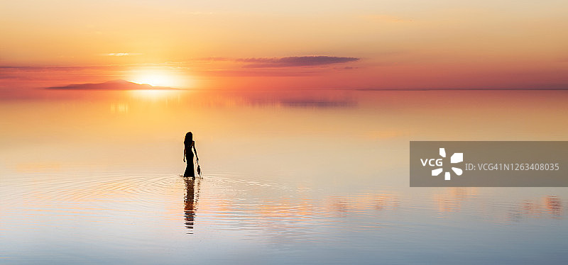 一个芭蕾舞女演员在湖上朝着太阳走去，穿着芭蕾舞鞋图片素材