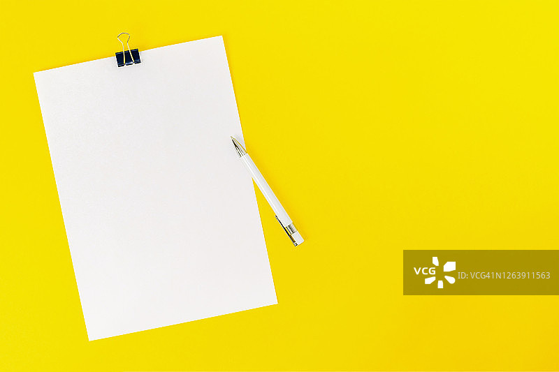 一张白纸用文具夹和一支钢笔固定在黄色背景上。模型，空白的董事会公告，信息，声明，学校。平的。图片素材