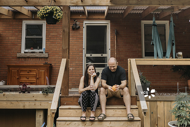 一对夫妇拿着饮料坐在屋外的台阶上聊天图片素材