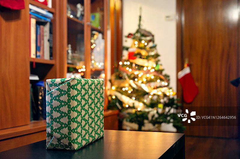 一个礼物包裹的特写与圣诞包装纸和圣诞树与它的灯在后面图片素材