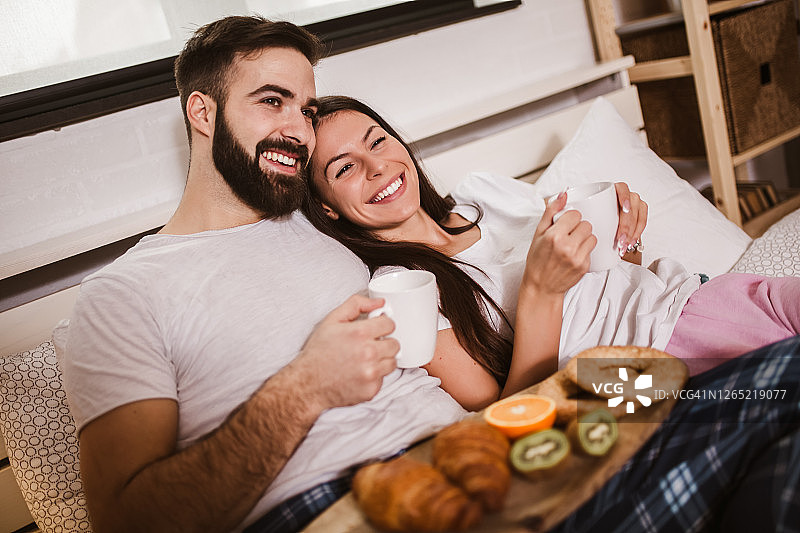 年轻幸福的夫妇早上在床上喝咖啡图片素材