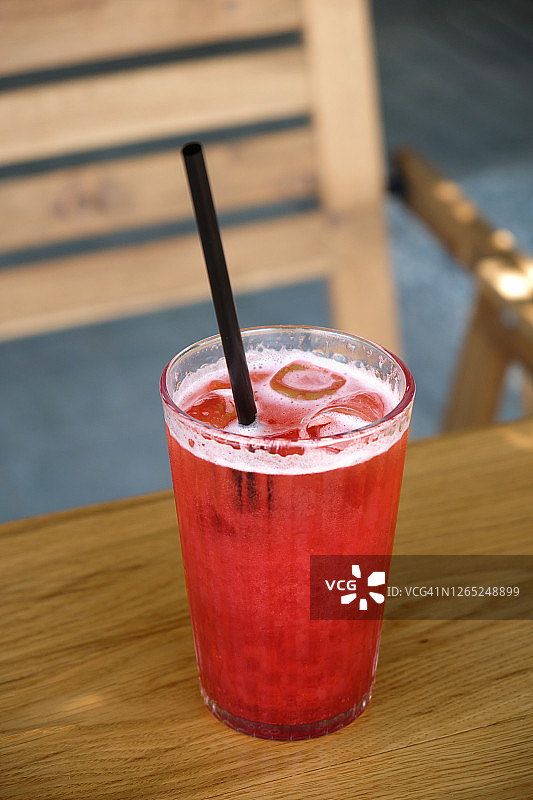 草莓软饮加冰，用玻璃杯装，放在街边咖啡馆或餐馆的木桌上。图片素材