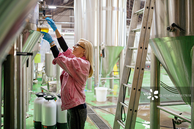 女子在啤酒厂将啤酒从容器中倒入玻璃以测试质量图片素材