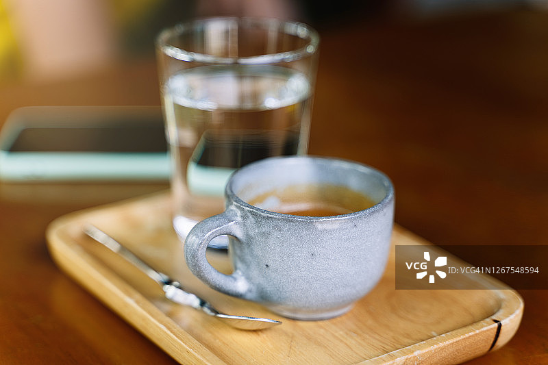 有选择地专注于一个盛满水的咖啡杯和一个放在木桌上的木盘子上的勺子图片素材