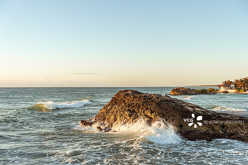 日出时分，加勒比海的海浪拍打着图卢姆海滩附近的岩石，背景是小屋和棕榈树图片素材