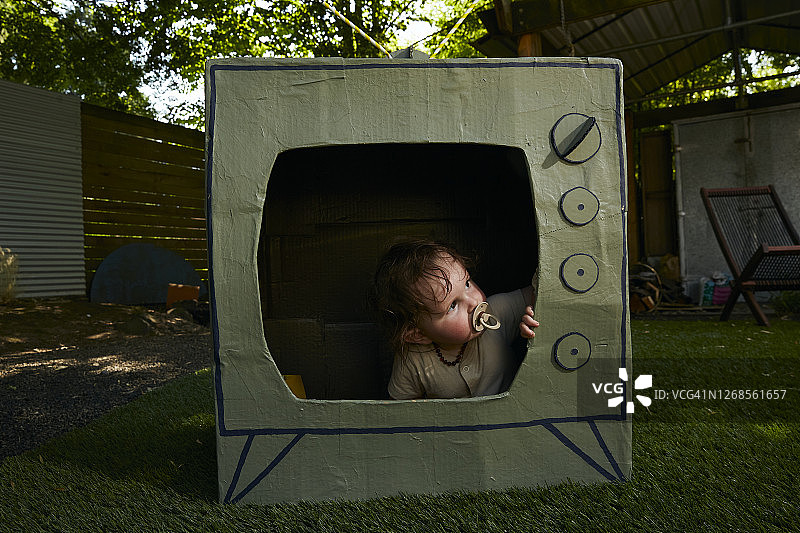 一个婴儿坐在纸制电视里向外看。图片素材