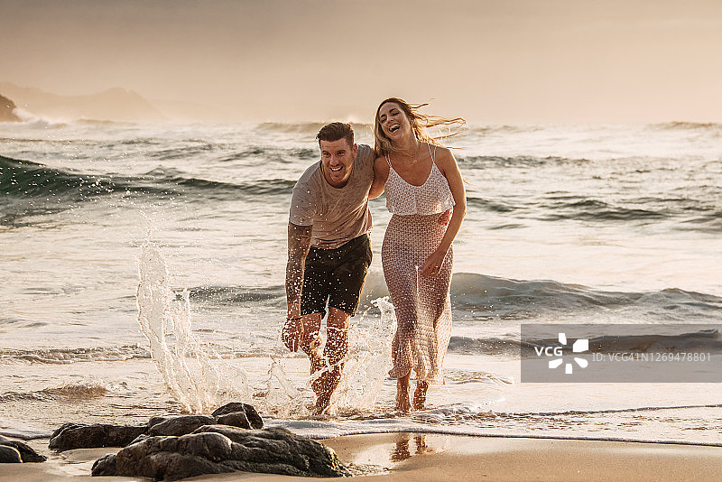 日落时分，一对幸福的年轻情侣在海滩上散步图片素材