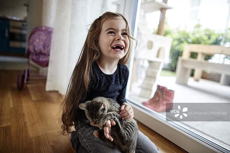 笑着的女孩坐在家里的地板上和可爱的小猫图片素材