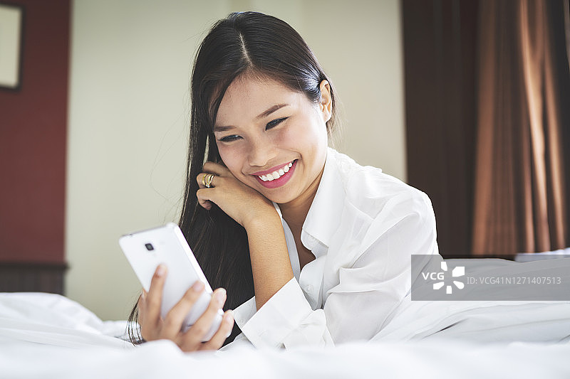一个年轻漂亮的亚洲女人在床上用手机图片素材