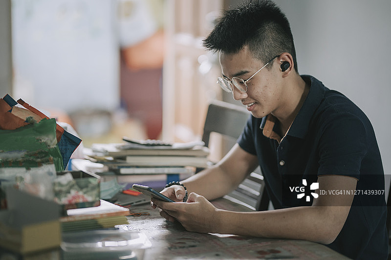 亚洲华人少年在家里用蓝牙耳机和智能手机听音乐图片素材