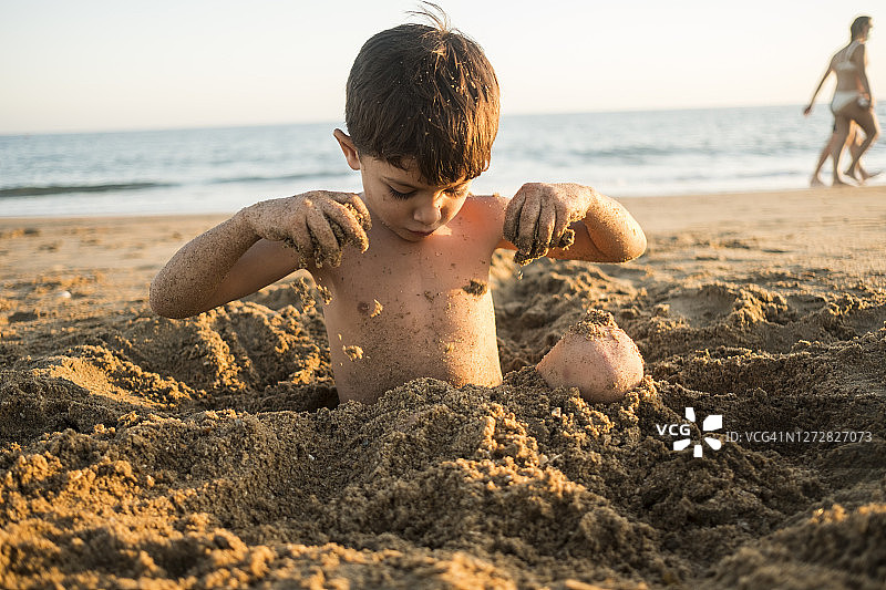 4岁的小男孩在沙滩上玩埋在沙子里的游戏图片素材