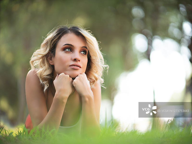 年轻漂亮的金发女人躺在户外的草地上图片素材