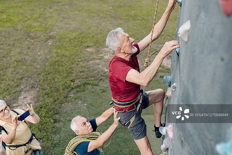 老人在朋友的支持下爬上运动攀岩墙图片素材