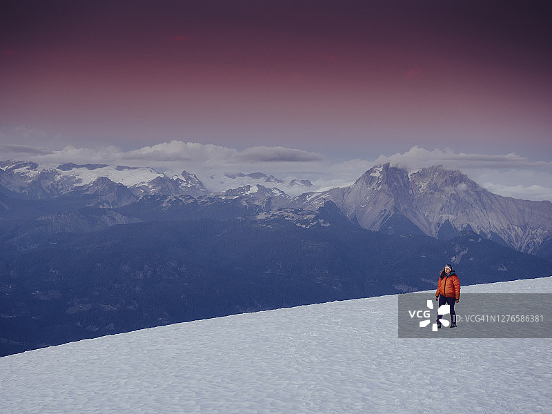 日落时分，一个孤独的女人在海岸山脉上白雪覆盖的冰川上行走图片素材