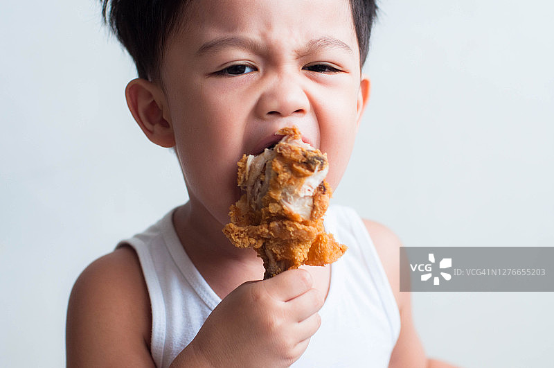 一个东南亚男孩正在吃炸鸡，背景是白色的图片素材