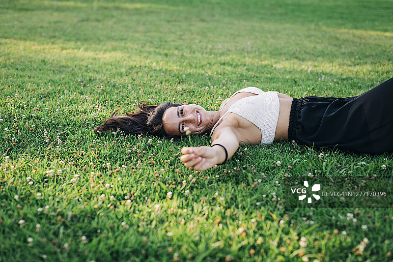 一位年轻女子手捧小花，躺在公园的草地上图片素材