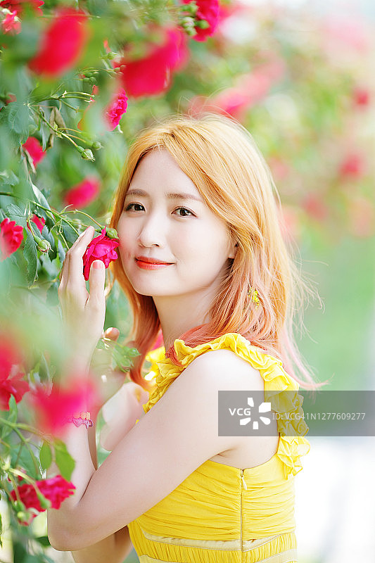 美丽的女孩穿着黄色的裙子站在玫瑰花园图片素材
