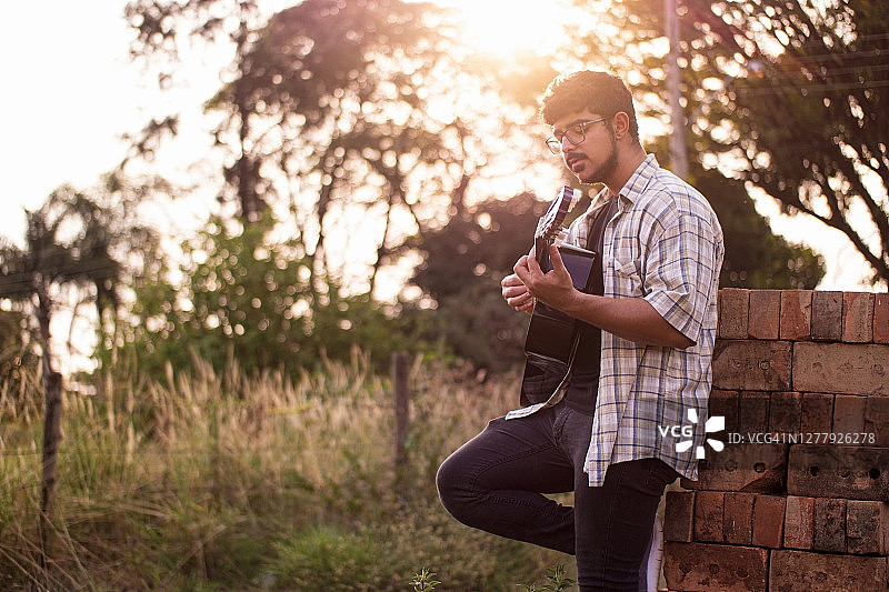 一个年轻人在乡下弹吉他。图片素材