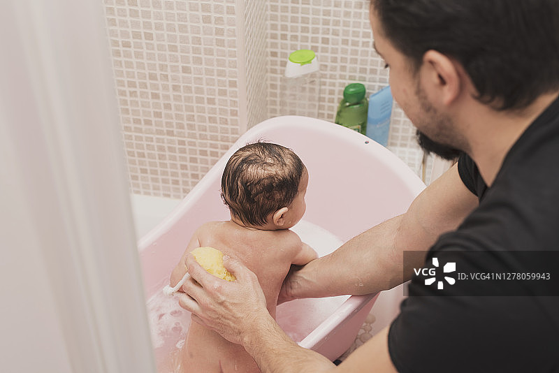 爸爸在小浴缸里给两个月大的宝宝洗澡。小男孩在洗澡。图片素材