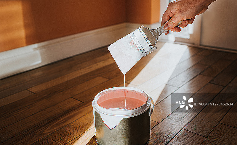 用手把油漆刷浸入一大罐粉红色油漆中，油漆慢慢滴回罐子里图片素材