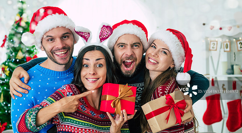 一群兴奋的美丽的朋友在圣诞老人的帽子有乐趣，而派对在家里的圣诞树背景图片素材