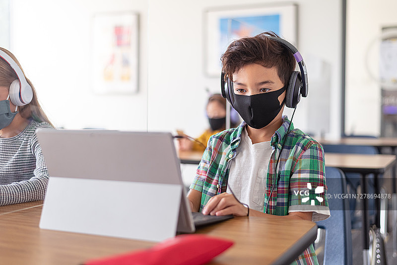 一名小学生戴着口罩在教室里使用平板电脑图片素材