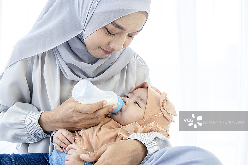 穆斯林母亲用奶瓶喂她的孩子。图片素材