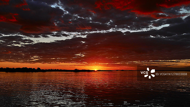 令人惊叹的多色日落与红色和橙色的天空和云倒映在水面上的丘比河游船，丘比国家公园。图片素材