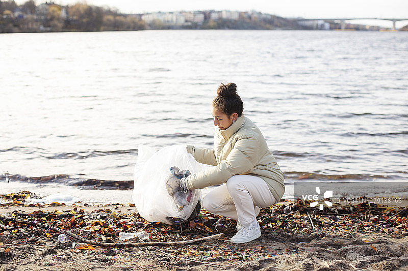 年轻的环保女性蹲在湖边收集垃圾图片素材