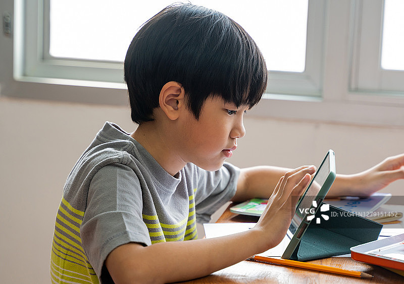 亚洲男孩在学校教室使用数字设备，数字原住民，技术，学习，触摸屏。男小学生在课堂上使用平板电脑图片素材
