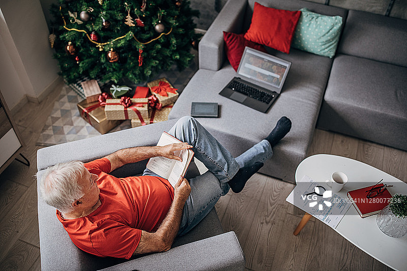 老人在家里的圣诞树旁看书图片素材
